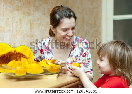Happy mother with girl cooks pumpkin in kitchen together. Focus on woman