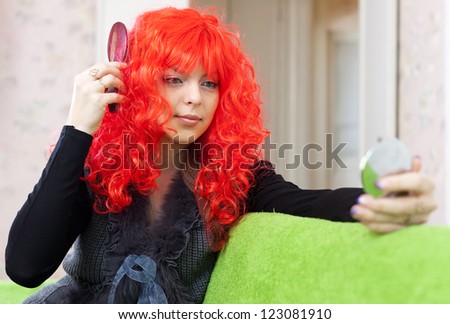 Woman in red peruke looks into mirror at home