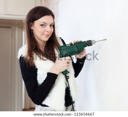 Young woman drill hole in the wall with a drill