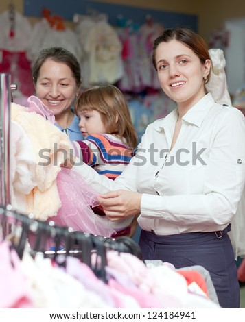 Happy women of three generations  chooses wear at children's clothes shop. Focus on woman