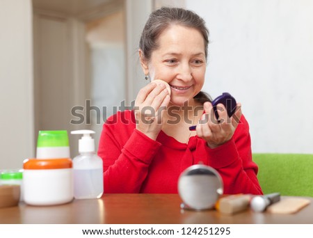 Smiling mature woman in red removes makeup from the face at home