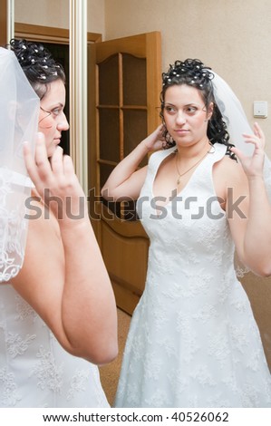 Beautiful bride in white before mirror at home