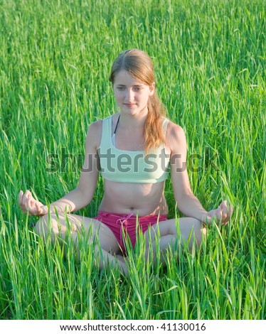 Beautiful young girl practicing yoga  against green grass