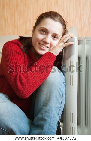 young smiling girl is sitting near oil heater