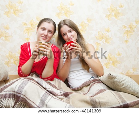 Two smiling girls have tea  in the bed at home