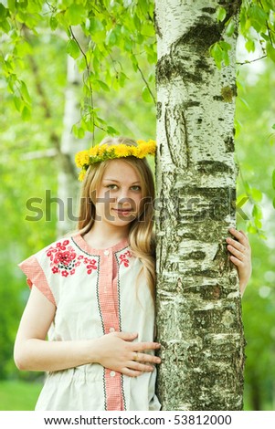 girl in flowers wreath and traditional clothes near birch