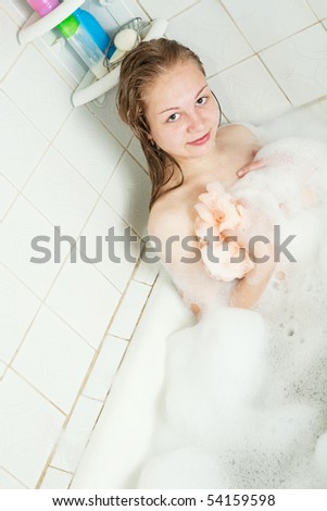 Long-haired girl washes with foam in bath
