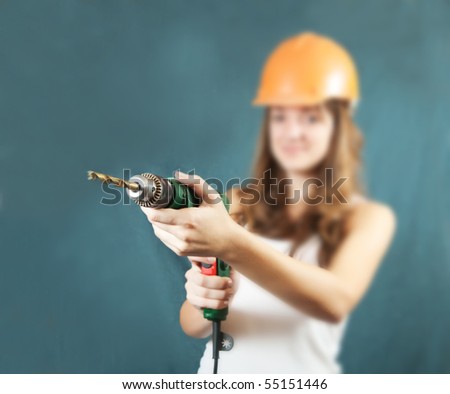 Female construction worker in a hard hat with drill over grey background. Focus on drill only