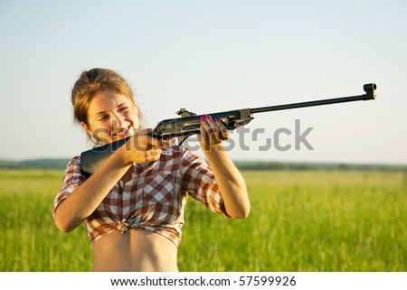 girl  aiming a pneumatic rifle  against summer field