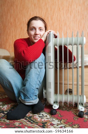young smiling girl is sitting near oil heater
