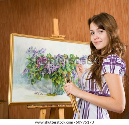 Girl with brushes near  easel with picture of flowers in interior