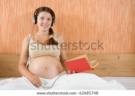 Happy pregnant woman reading and listening to music at home