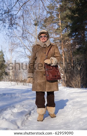 senior  woman in sheepskin coat goes for a walk on the wintry forest
