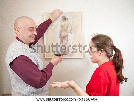 An attractive young man and her wife attempting to hang an art picture