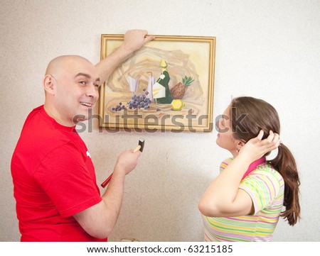 An attractive young man and her wife attempting to hang an art picture