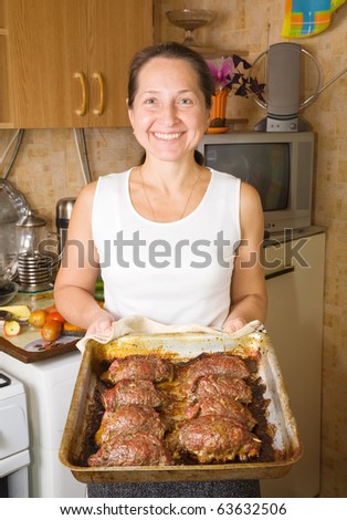 Mature woman with cooked baked beef on cook griddle in kitchen. One of the stages of preparation of  stuffed beef.  See series