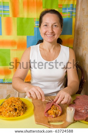 Mature woman sewing  stuffed beef by toothpicks  in her kitchen. One of the stages of preparation of the stuffed beef.  See series