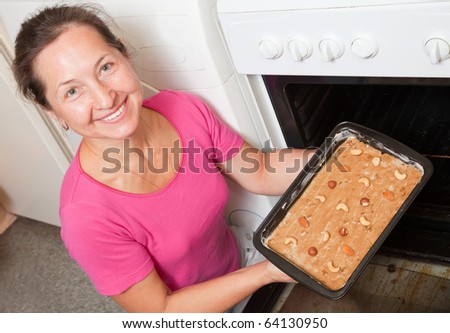 Mature woman puts dough on roasting pan into oven. One of the stages of cooking of  honey cake.  See series