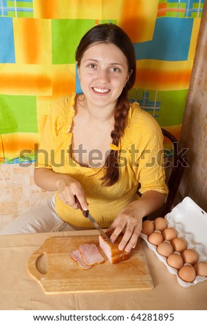 Young woman cutting bacon on cutting board in her kitchen. One of the stages of preparation of bacon and eggs.  See series