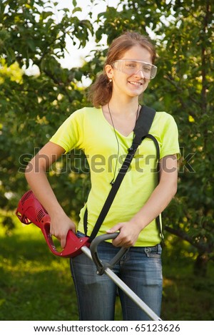 Girl works with cordless grass trimmer in garden