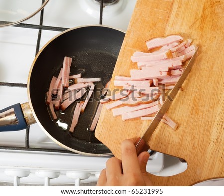 Closeup of  cook hands adds sliced bacon to hot skillet. One of the stages of preparation of bacon and eggs.  See series