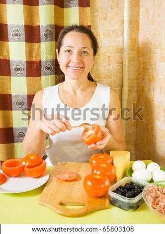 Mature woman making stuffed tomato in her kitchen. See in series stages of cooking of farci tomato