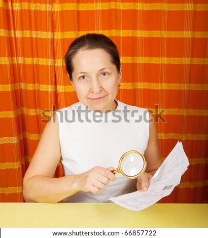 mature woman looking at utility bills through  magnifier