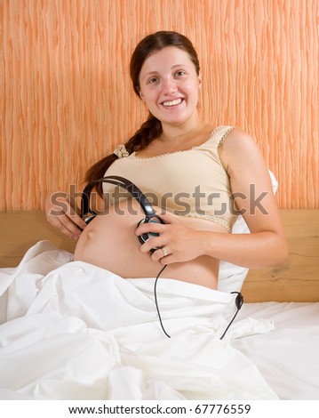 pregnant woman with headphones on tummy with relaxing music playing for baby in womb