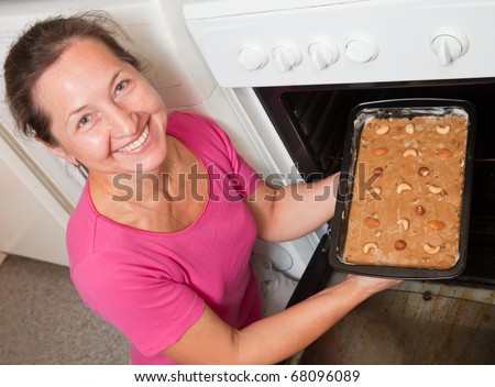 Mature woman putting dough on roasting pan into oven. One of the stages of cooking of  honey cake.  See series