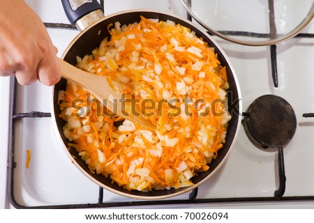 Closeup of roasting mixed onion and carrot on gas stove. One of the stages of preparation of the stuffed beef.  See series