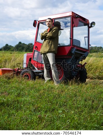 Farmer with tractor on meadow grass in summer day