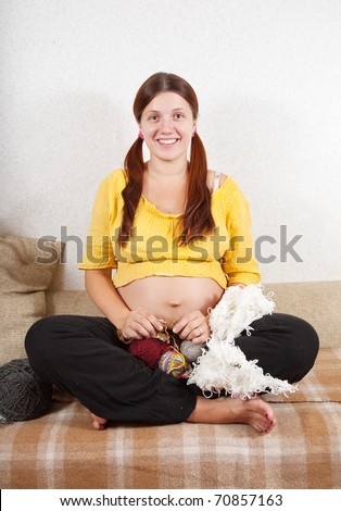 9 months pregnant woman knitting with knitting-needle on sofa at home