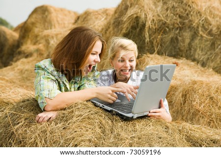 Happy country girls with laptop on  hay at field