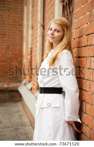 Pretty girl in white cloak near red brick house