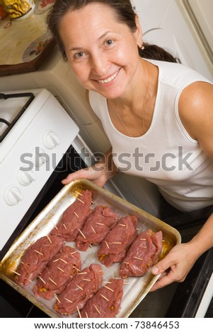 Mature woman putting stuffed beef on roasting pan into oven. One of the stages of preparation of the stuffed beef.  See series