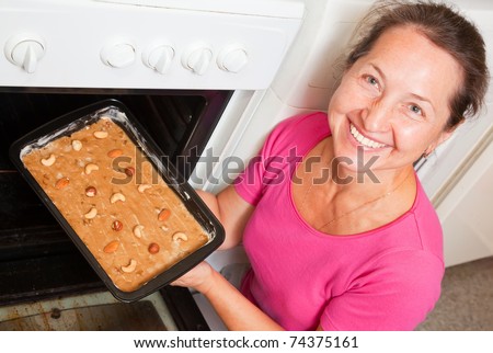 Mature woman putting dough on roasting pan into oven. One of the stages of cooking of  honey cake.  See series