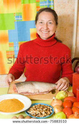 Mature woman is cooking red  fish  in kitchen