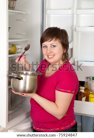 Young woman with pan and spoon near refrigerator  at home