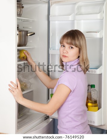 Young woman taking green apple  from refrigerator  at home