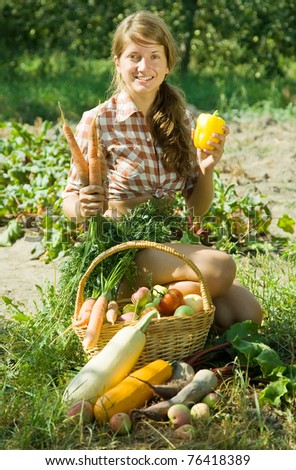 Cheerful girl sitting near basket of harvested vegetables and fruits