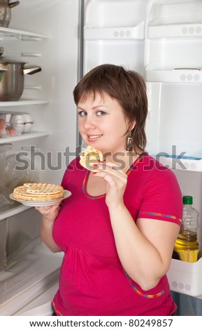 Young woman eating  scone from refrigerator at home