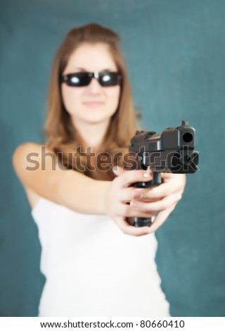 Long-haired  girl in sunglasses aiming a black gun. Focus on gun only