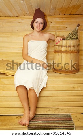 girl in white sheet sits on bench in sauna