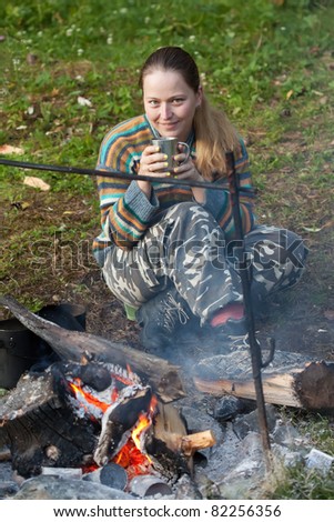 Female tourist drinking tea  at camp near fire