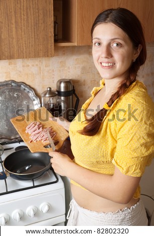 Young woman adds sliced bacon to hot skillet. One of the stages of preparation of bacon and eggs.  See series