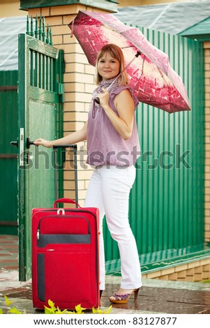 Happy woman with  luggage near fence wicket  in front of home