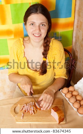 Young woman cutting bacon on cutting board in her kitchen. One of the stages of preparation of bacon and eggs.  See series