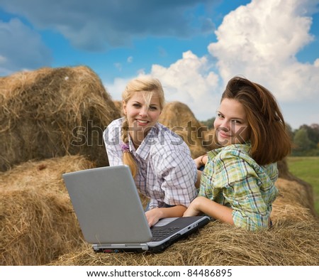 country girls resting with laptop on fresh hay bale