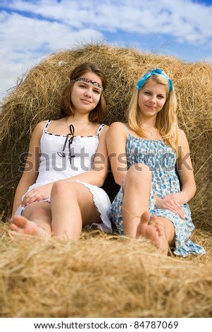Pretty girls in dresses resting on hay bale