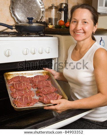 Mature woman roasting stuffed beef on pan in oven. One of the stages of preparation of  stuffed beef.  See series